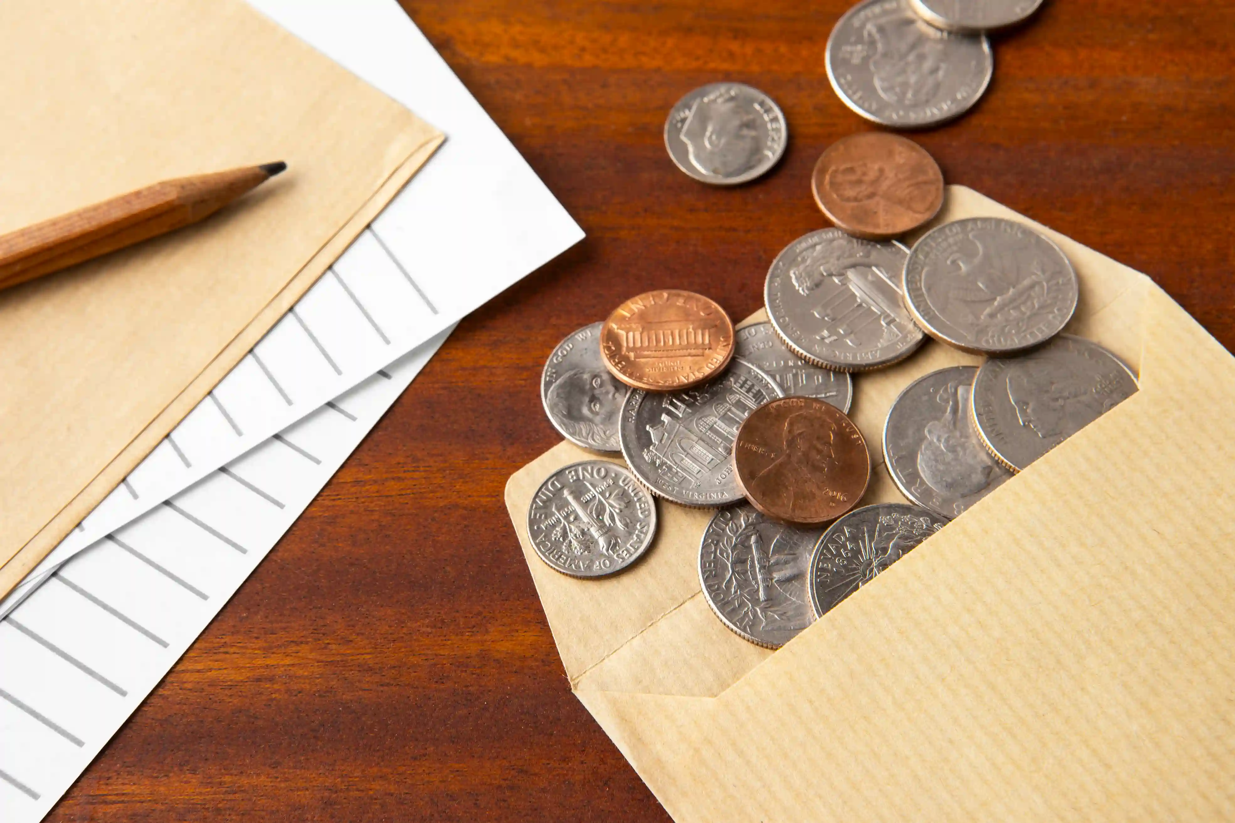 close-up coins in an envelope on a table next to a pencil and different papers